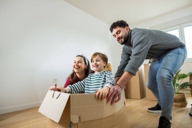 Neşeli bir çift ve yeni yürümeye başlayan çocukları, parlak, ferah bir odada bir sürü karton kutu arasında taşınma gününü kutluyorlar..