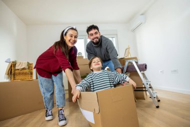 Neşeli bir çift ve yeni yürümeye başlayan çocukları, parlak, ferah bir odada bir sürü karton kutu arasında taşınma gününü kutluyorlar..