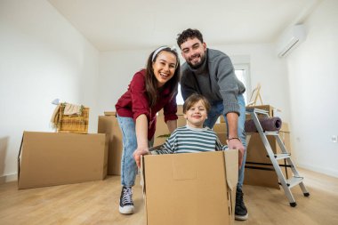 Neşeli bir çift ve yeni yürümeye başlayan çocukları, parlak, ferah bir odada bir sürü karton kutu arasında taşınma gününü kutluyorlar..