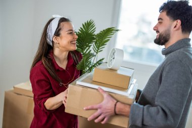 Neşeli bir adam ve kadın ellerinde karton kutularla birbirlerine bakıp gülüyorlar ve ilk dairelerine taşınmalarının heyecanını kutluyorlar..