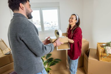 Neşeli bir adam ve kadın ellerinde karton kutularla birbirlerine bakıp gülüyorlar ve ilk dairelerine taşınmalarının heyecanını kutluyorlar..