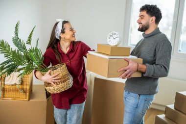 Neşeli bir adam ve kadın ellerinde karton kutularla birbirlerine bakıp gülüyorlar ve ilk dairelerine taşınmalarının heyecanını kutluyorlar..