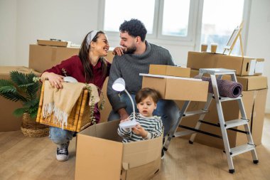 Genç bir aile taşınma gününde, bir anne çocuğuyla karton bir kutunun içinde oynarken baba arka plandaki taşınmayı yönetir.