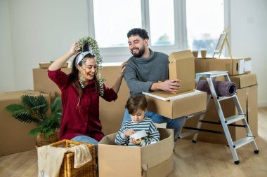 Taşınırken bir çifti ve oğullarını gösteren, çoklu görev ve taşınmanın heyecanını yakalayan parlak, modern bir apartman sahnesi..