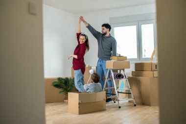Neşeli bir adam ve kadın taşınma gününü boş, güneşli oturma odalarında dans ederek kutluyorlar. Küçük çocukları hareket halindeki bir kutuda oturuyor ve gülüyor.