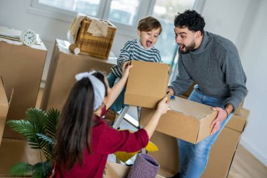 Genç bir anne, baba ve küçük oğulları parlak, boş oturma odalarında kutuları taşıyorlar. Ebeveynler daha büyük kutular taşırken, küçük çocuk gururla anne ve babasını taklit ederek küçük bir kutu taşıyor..