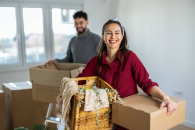 Yeni dairesinde, elinde küçük bir karton kutuyla kameraya gülümseyen genç bir annenin canlı bir portresi. Bulanık arka planda, kocası ve küçük oğlu görülebiliyor ve aile kavgasına içerik katıyor.