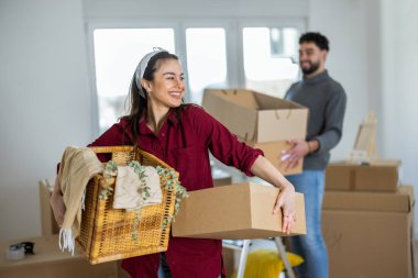 Yeni dairesinde, elinde küçük bir karton kutuyla kameraya gülümseyen genç bir annenin canlı bir portresi. Bulanık arka planda, kocası ve küçük oğlu görülebiliyor ve aile kavgasına içerik katıyor.