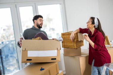 Neşeli bir adam ve kadın, karton kutularla çevrili, parlak, modern bir iç mekanda, birlikte kutuları açma sürecinin tadını çıkarıyorlar..