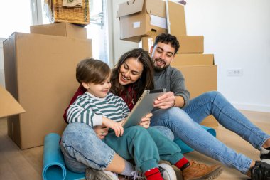 Neşeli bir anne, baba ve oğul komik bir anı paylaşıyor ya da kutuları açarken dijital fotoğrafları bir cihazda görüyorlar..