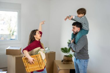 Neşeli genç bir çift ve küçük oğulları taşınmanın ortasındalar. Anne karton kutular tutarken, gülümseyen baba oğlunu omuzlarına alıyor..