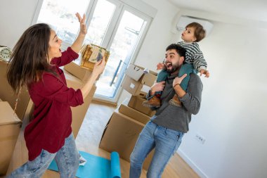 Taşınırken neşeli bir çocuğun babasının omuzlarına oturduğu, annesinin akıllı telefonuyla fotoğraf çekerken güldüğü samimi bir an. Etrafı karton kutularla çevrili yeni dairelerinde yeni bir başlangıcın saf eğlence ve heyecanını yakalıyorlar.