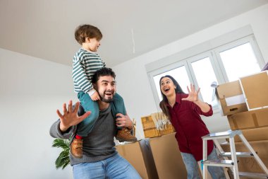 Yeniden yerleştirme sırasında neşeli bir çocuğun babasının omuzlarına oturduğu, her iki ebeveynin de aptal suratları yaparken kahkahalarla güldüğü samimi bir an. Karton kutularla çevrili..