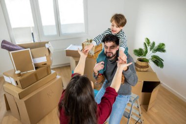 Bir anne, baba ve oğulun yeni evlerindeki ilk günlerinde anılarını yarattıkları şefkatli ama neşeli bir an. El ele tutuşup hayali bir ritimle hareket ediyorlar. Çocuk babasının omuzlarında güvende..