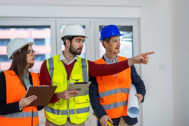 Güvenlik yelekleri ve kasklı bir grup işçi iç duvara bakıyor. Diğerleri izlerken bir işçi işaret ediyor. Denetleme ve yenileme planlama kavramı.
