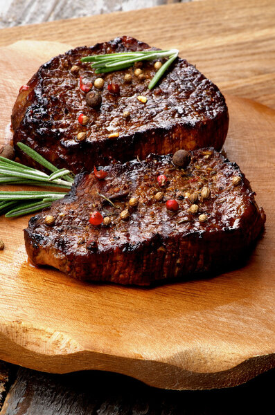 Gourmet Roasted Beef Steaks with Spices and Rosemary on Wooden Plate on Rustic Wooden background