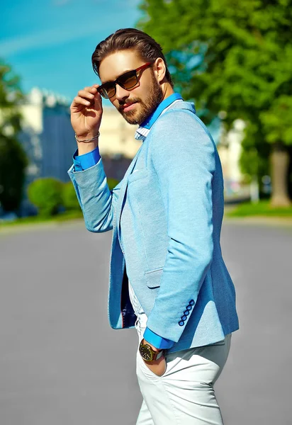 High fashion look. Ung snygg säker glad stilig affärsman modell man i blå kostym trasa livsstil i gatan bakom himlen i solglasögon — Stockfoto