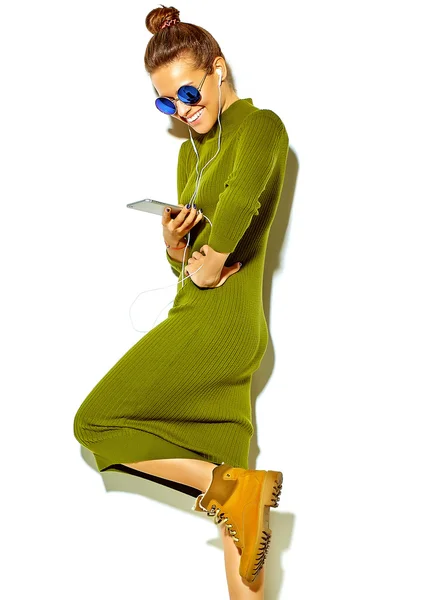 Retrato de hermosa chica morena sonriente linda feliz en ropa de verano hipster azul casual sin maquillaje aislado en blanco en gafas de sol escuchando música en el teléfono inteligente con auriculares — Foto de Stock