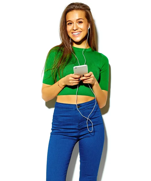 Portrait de belle folle souriante femme brune fille en vert décontracté hipster vêtements d'été sans maquillage isolé sur blanc dans les lunettes de soleil écouter de la musique dans le smartphone avec écouteurs — Photo