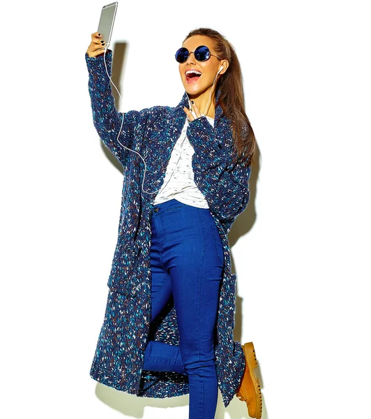 Retrato de hermosa chica morena sonriente linda feliz en ropa de verano hipster azul casual sin maquillaje aislado en blanco en gafas de sol escuchando música en el teléfono inteligente con auriculares — Foto de Stock