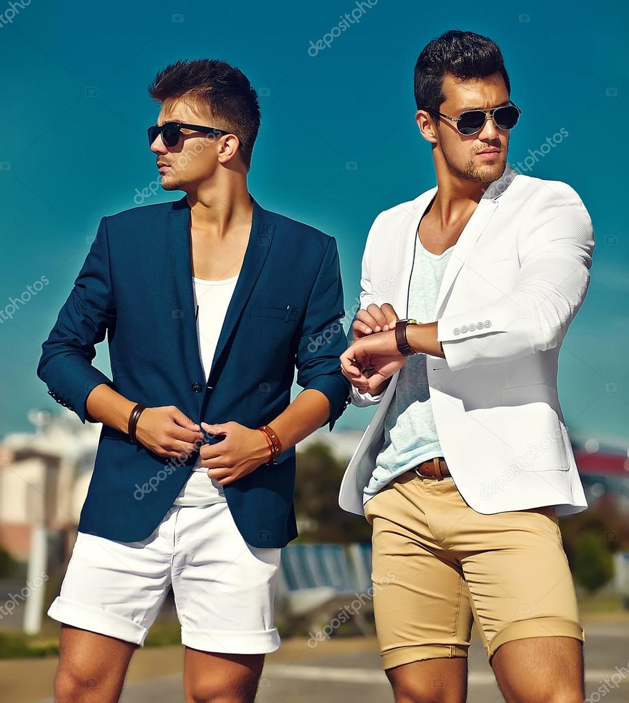 Fashion portrait of two young sexy handsome men models in casual cloth suit in sunglasses in the street behind blue sky