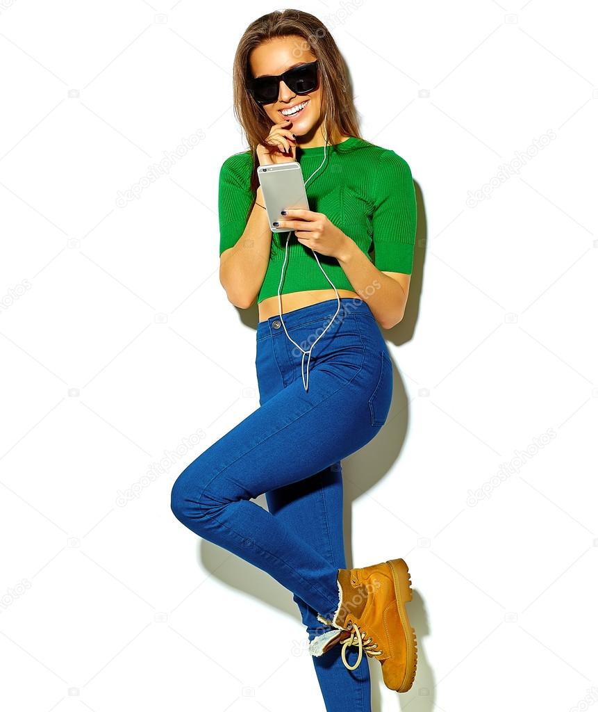 portrait of beautiful crazy smiling brunette woman girl in casual green hipster summer clothes with no makeup isolated on white in sunglasses listening music in smartphone with headphones