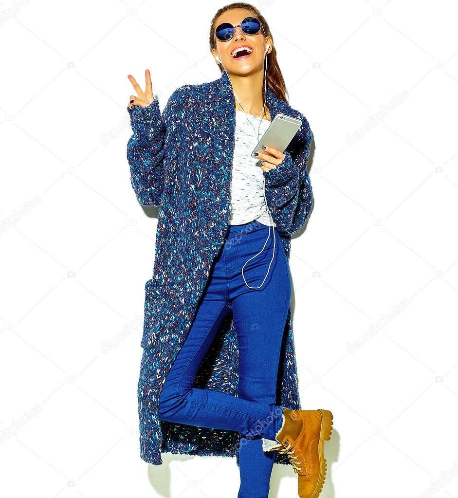 portrait of beautiful happy cute smiling brunette woman girl in casual blue hipster summer clothes with no makeup isolated on white in sunglasses listening music in smartphone with headphones showing peace sign