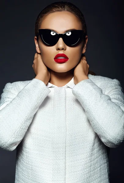 Alta moda look.glamor hermosa sexy elegante modelo mujer joven morena con labios rojos en chaqueta de abrigo blanco en gafas de sol — Foto de Stock