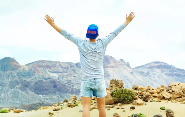 Feliz hombre elegante en ropa hipster casual de pie en el acantilado de la montaña con las manos levantadas al sol y celebrando el éxito — Foto de Stock