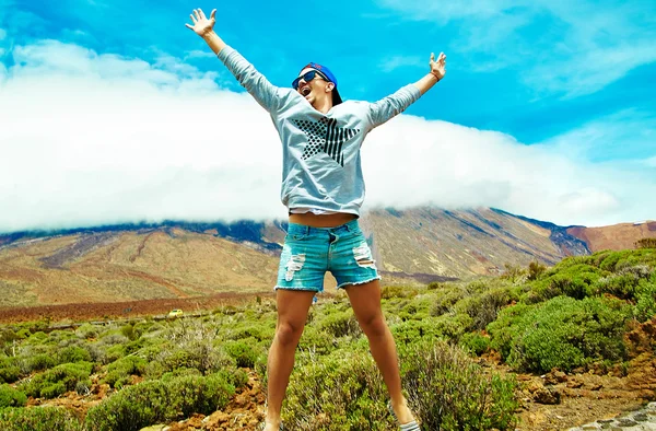 Happy stylish man in casual hipster clothes jumping in front of mountain with raised hands to the sun and celebrating success — Stock Photo, Image