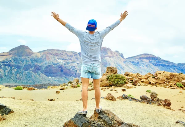 Feliz hombre elegante en ropa hipster casual de pie en el acantilado de la montaña con las manos levantadas al sol y celebrando el éxito — Foto de Stock