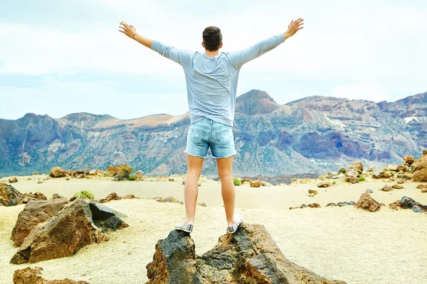 Feliz hombre elegante en ropa hipster casual de pie en el acantilado de la montaña con las manos levantadas al sol y celebrando el éxito —  Fotos de Stock
