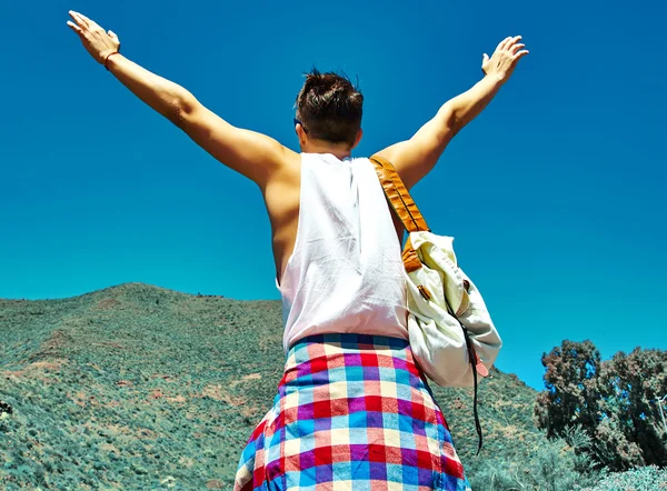 Homem elegante feliz em roupas hipster casuais pulando na frente da montanha com as mãos levantadas para o sol e celebrando o sucesso — Fotografia de Stock