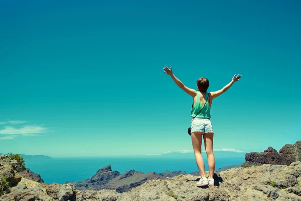 Mujer chica con estilo feliz en ropa hipster casual de pie en el acantilado de la montaña con las manos levantadas al sol y celebrando el éxito —  Fotos de Stock