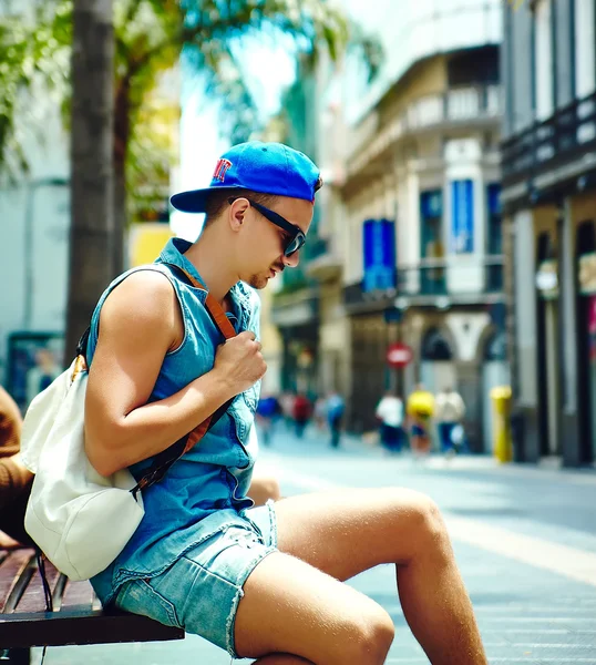 Молодой стильный мужчина в отпуске, путешествуя по европейскому городу, сидя на скамейке запасных — стоковое фото