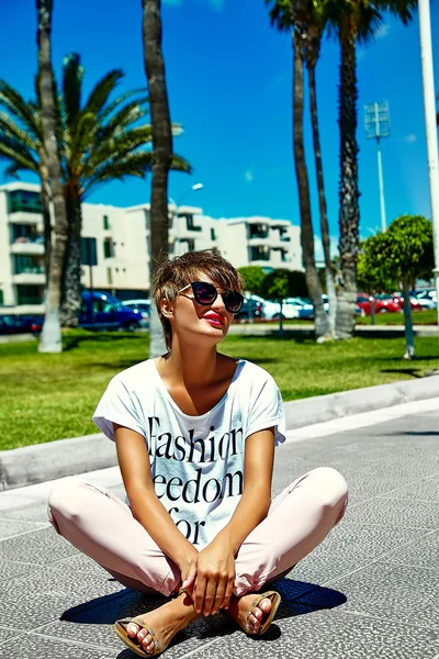 Portret van mode sexy hete mooie jonge brunette vrouw model in zomer hipster stijlvolle moderne kleding zittend in de straat — Stockfoto