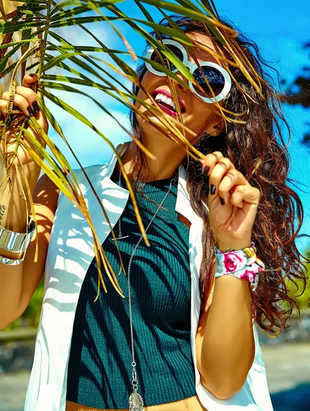 Fashion stylish beautiful young smiling brunette woman model in summer hipster casual clothes posing near palm leafe tree — Stock Photo, Image