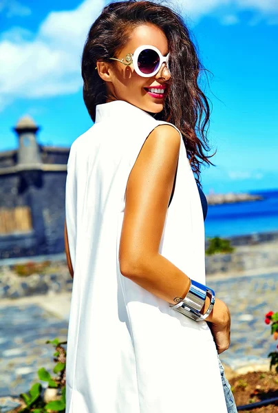 Porträtt av vackra leende sexig brunett affärskvinna modell i vita kläder i solglasögon poserar bakom blå himmel — Stockfoto