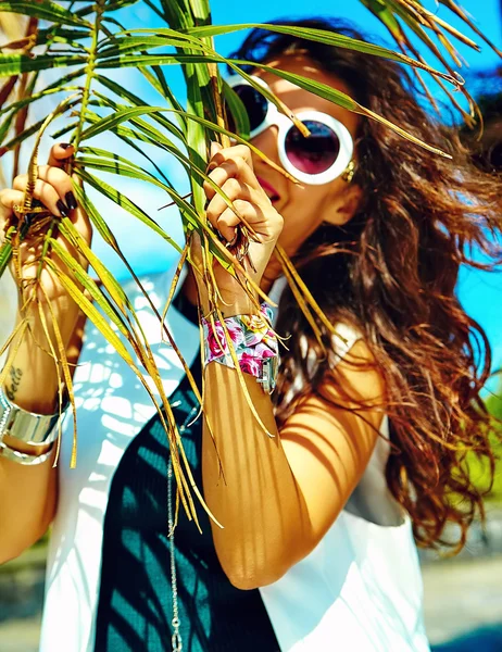 Fashion stylish beautiful young smiling brunette woman model in summer hipster casual clothes posing near palm leafe tree — Stock Photo, Image