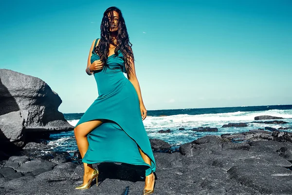 Aspecto de alta moda. hermosa sexy elegante morena sonriente joven modelo posando al aire libre en estilo de moda en la noche vestido largo azul detrás del cielo y el océano azul —  Fotos de Stock