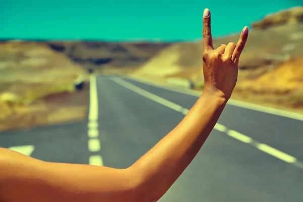 Jóvenes turistas caucásicos haciendo autostop a lo largo de un camino al atardecer y mostrando un cartel de rock and roll —  Fotos de Stock