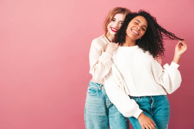 İki güzel, güzel, gülümseyen uluslararası hippi kadın, son moda yaz kot kıyafetleri içinde. Stüdyoda pembe duvarın yanında poz veren kaygısız seksi kadınlar. Pozitif modeller eğleniyor. Arkadaşlık kavramı 