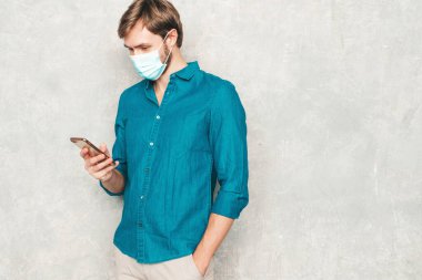 Yakışıklı, gülümseyen hippi, keresteci iş adamının portresi. Günlük kot gömlek giyiyor. Stüdyoda gri duvara karşı poz veren modacı. Cep telefonu ekranına bakıyor, uygulamalar kullanıyor.