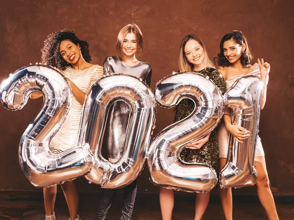 Beautiful Women Celebrating New Year.Happy Gorgeous Female In Stylish Sexy Party Dresses Holding Silver 2021 Balloons, Having Fun At New Year\'s Eve Party. Holiday Celebration.Charming Models