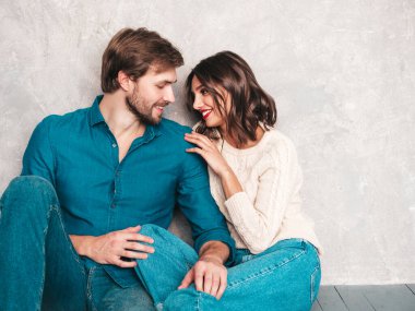 Gülümseyen güzel kadın ve yakışıklı erkek arkadaşı. Mutlu mutlu aile stüdyoda gri duvarın yanında oturuyor. Sevgililer Günü. Mankenler sarılıyor. Aşk kavramı. Birbirinize bakın.