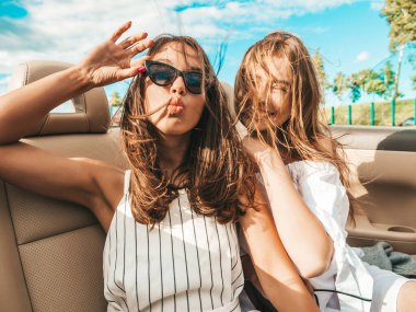 Üstü açık arabadaki iki güzel ve gülümseyen hippi kadının portresi. Cabriolet kullanan kaygısız seksi kadınlar. Pozitif modeller güneş gözlükleriyle geziyor ve eğleniyorlar.