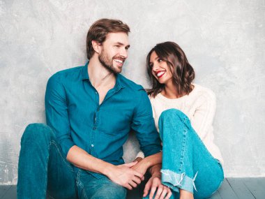 Gülümseyen güzel kadın ve yakışıklı erkek arkadaşı. Mutlu mutlu aile stüdyoda gri duvarın yanında oturuyor. Sevgililer Günü. Mankenler sarılıyor. Aşk kavramı. Birbirinize bakın.