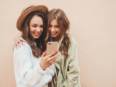 İki güzel, gülümseyen hippi kadın. Sokakta şapkalarla poz veren kaygısız seksi kadınlar. Modeller eğleniyor. Cep telefonu ekranına bakıp gülüyorlar. Mobil uygulamalar kullanarak eğleniyorlar.