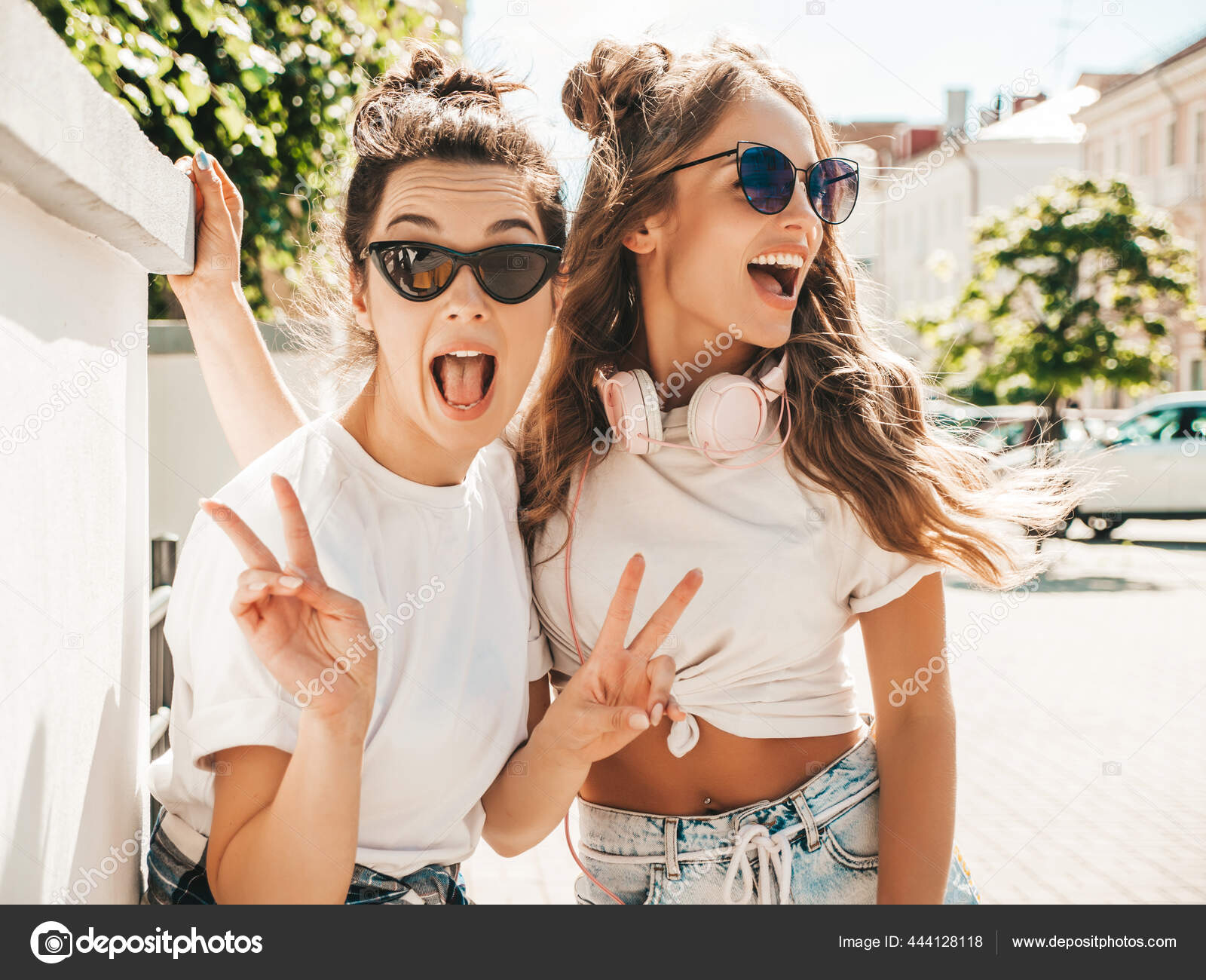 两个年轻美丽的嬉皮士女性穿着时髦的夏季白色t恤衫的肖像性感无忧无虑的女性在街上摆出背景拥抱和发疯的正面模特 两个年轻美丽的嬉皮士女性穿着时髦的夏季白色t恤衫的肖像性感无忧无虑的女性在街上摆出背景拥抱和发疯的正面模特