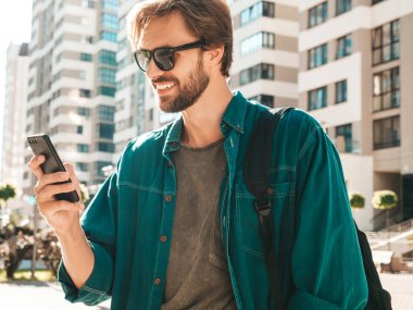 Yakışıklı, şık, havalı, lamberseksüel bir model. Tişört giymiş bir adam. Beyaz duvarın yanında sokakta poz veren bir erkek. Cep telefonunda tutuyor, kaydırıyor ve mesaj atıyor. Akıllı telefondan mesaj yazar